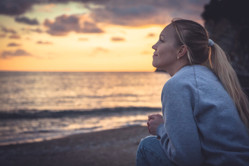 Individual therapy page image with a Pensive lonely smiling woman looking with hope into horizon during sunset at beach
